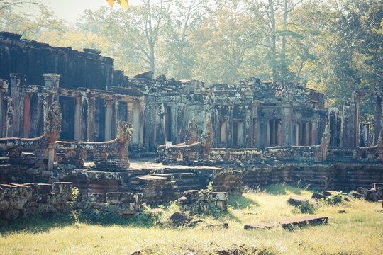 Ancient Khmer temple ruins with weathered columns and naga balustrades under soft morning light in a forest setting.