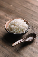 Steamed White Rice in Ceramic Bowl with Wooden Spoon on Rustic Wooden Table – Asian Food Close-Up, Bowl of Fluffy Cooked Jasmine Rice with Traditional Spoon on Wooden Surface.