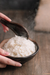 Steaming Hot White Rice in Ceramic Bowl with Wooden Spoon – Close-Up Hand Serving Traditional...