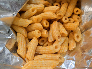 Crispy, tube-shaped snacks with a light beige hue fill an opened foil bag.
