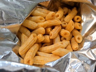 Crispy, tube-shaped snacks with a light beige hue fill an opened foil bag.