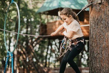 Little cute girl child having fun at adventure park. Kids climbing in a rope park. Children summer...