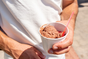 Man holding cup with scoop of sweet dessert chocolate ice cream in hand