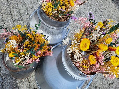 Drei alte Milchkessel, gef&uuml;llt und dekoriert mit vielen bunten Trockenblumen Gestecke