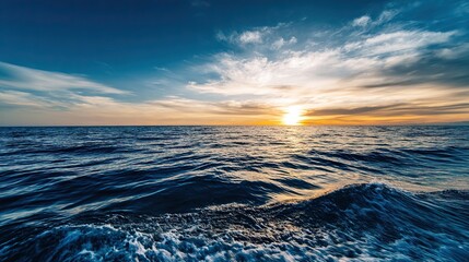 Obraz premium Vast sea with setting sun shining on endless water surface, blue sky with white clouds on the horizon, and ripples rising from deep ocean bottom, forming a magnificent natural landscape.