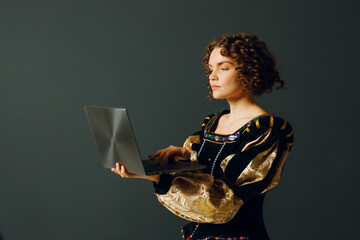 Portrait of a young aristocratic woman dressed in a medieval dress working on laptop