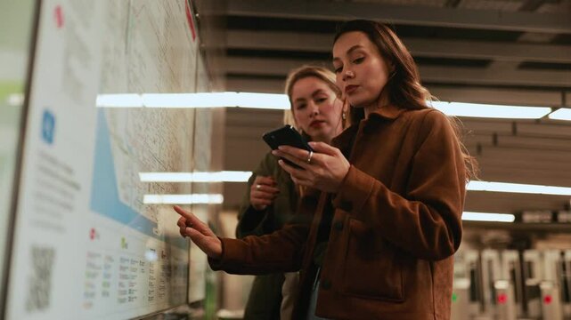 Two female friends are looking at the map and the phone that one of them is holding while they are talking