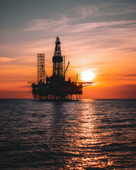 Obraz premium An oil rig silhouette against a sunset over the sea -