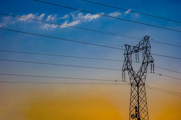 High voltage power towers and lines under the background of blue sky, white clouds, and orange sunlight