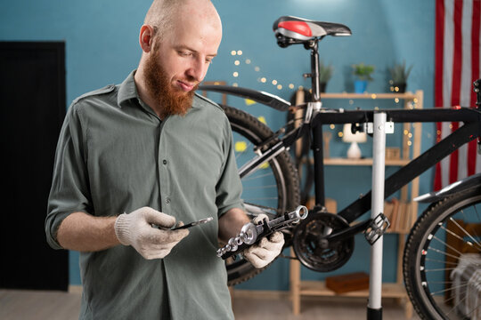 Bearded Cyclist Repairing Bicycle at Home Selecting Wrenches for Maintenance Work - Powered by Adobe