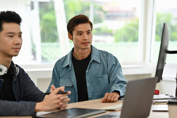 Two young creative professionals discussing ideas in a bright modern office, brainstorming around...