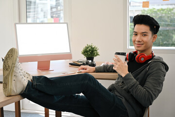 A Confident Young male graphic designer relaxing at the workplace with a cup of coffee, casual...