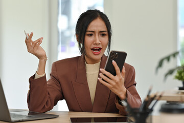 Young businesswoman expressing anger and frustration while arguing on a smartphone call,...