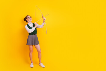 Smiling teenage student holding a bow and arrow against a vibrant yellow background, symbolizing...
