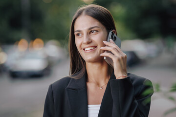Elegant smiling business woman talking by smartphone in the city