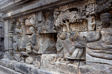 Ancient stone relief showing people, trees, and intricate carvings on a temple wall.