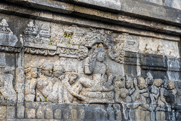 A stone relief shows a seated figure surrounded by followers in detailed ancient temple carvings.