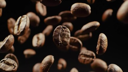 Roasted coffee beans falling against a black background.