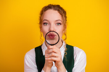 Young woman with magnifying glass displaying curiosity against vibrant yellow backdrop, symbolizing...