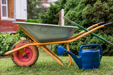 A garden wheelbarrow, rake, and watering can in the backyard of a house. The concept of gardening...