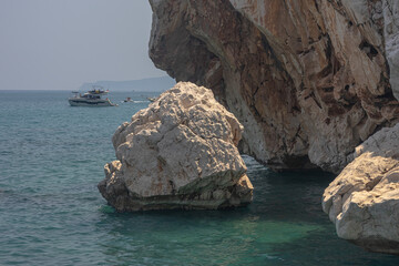 Yacht holidays in the Mediterranean Sea. In the sea, near the rocks, people relax on yachts. A sea boat is visible next to the rock. In summer, people relax on a yacht in the sea next to large rocks.