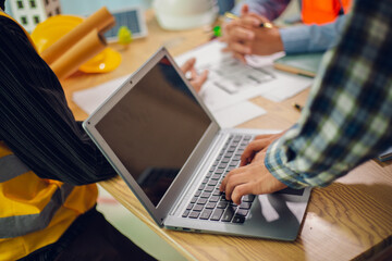 Engineers and architects discuss and consider construction plans for new renewable energy project in office with design documents, laptop and hard hat on table. Concept of engineers and architects+