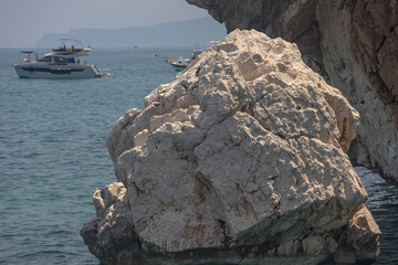 Yacht holidays in the Mediterranean Sea. In the sea, near the rocks, people relax on yachts. A sea boat is visible next to the rock. In summer, people relax on a yacht in the sea next to large rocks.