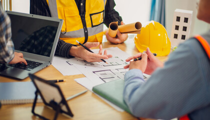 Engineers and architects discuss and consider construction plans for new renewable energy project in office with design documents, laptop and hard hat on table. Concept of engineers and architects+