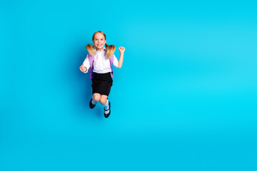 Obraz premium Energetic young schoolgirl enjoying a moment of joy, jumping against a vibrant blue background in her school uniform