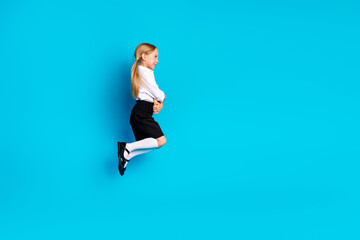 Charming young schoolgirl jumping joyfully in a school uniform against a bright blue background