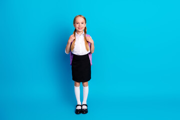 Smiling young girl in school uniform on blue background ready for school showcasing happiness and...