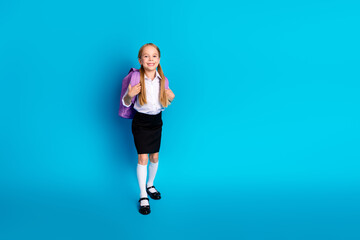 Cheerful young student with her backpack against a vibrant blue background, ready for a new day of...