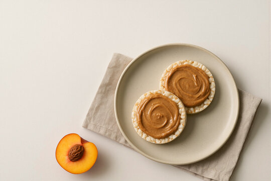 Rice cakes topped with peanut butter next to a fresh peach  