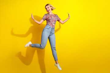 Stylish young woman in a casual outfit jumping against a vibrant yellow background with a cheerful pose and energy