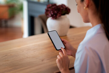 Woman sitting at a table and using a blank screen mobile phone