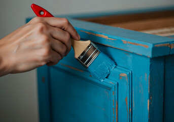 Close-up of a hand painting vintage wooden furniture with light blue brush-on paint