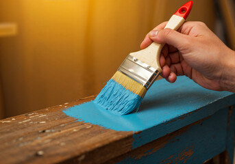 Close-up of a hand painting vintage wooden furniture with light blue brush-on paint