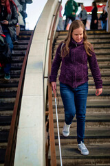 Full length of a visually impaired woman with white cane walkin down the stairs outside