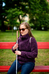 A visually impaired woman with white cane sitting in a city park and relaxing