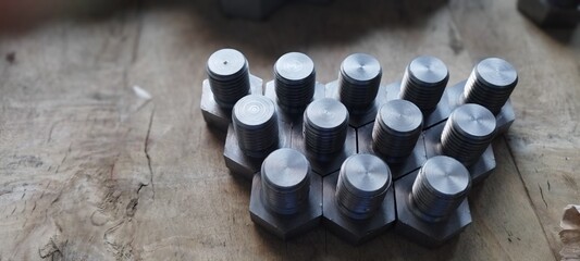 Close-up of a group of metal hex bolts arranged on a wooden surface.  Hex head bolts arranged in a...
