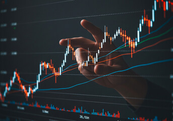 Professional hand points at detailed financial market analysis on a computer monitor in an office setting.