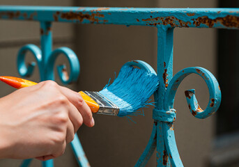 Close-up of brush applying glossy blue paint on a rusty iron railing