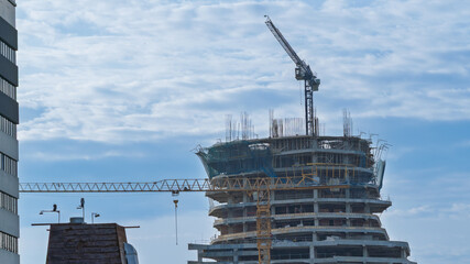 Skyscraper under construction with tower cranes and visible curved structure. Urban scene of modern architectural development.