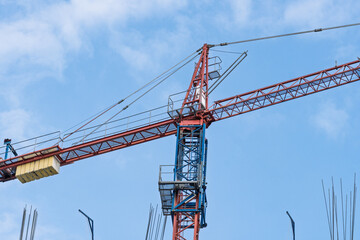 Red and blue tower crane at construction site. Detailed view of heavy machinery and urban steel structure.