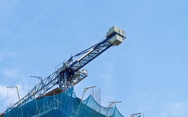 Blue tower crane on building under construction with safety net. Engineering and urban development...