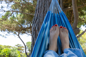 Close-up of women's feet with red pedicure relaxing in a hammock in nature