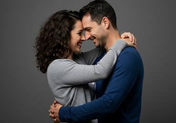 Smiling couple embracing with foreheads touching against a gray background