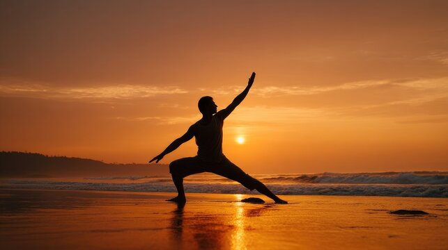 Male silhouette performing yoga warrior pose on wet beach sand during golden sunset. Peaceful meditation scene with ocean waves and orange sky creating dramatic evening atmosphere