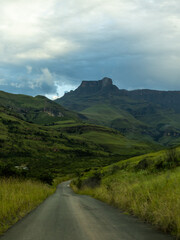 Road leading into the Drakensberg mountains with a peak rising in the background, in shadow from...