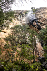 Looking up below a small waterfall, tumbling down a steep sandstone cliff.